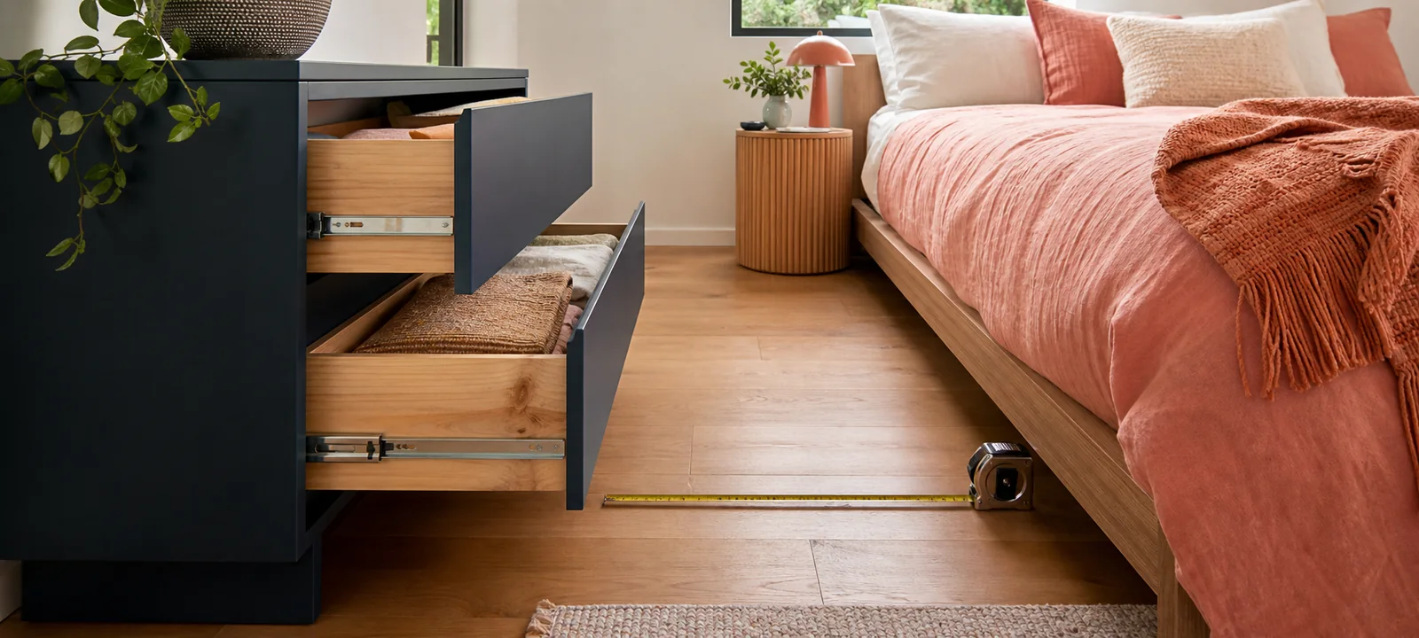 A calm bedroom with a timber dresser, folded clothes and warm natural light