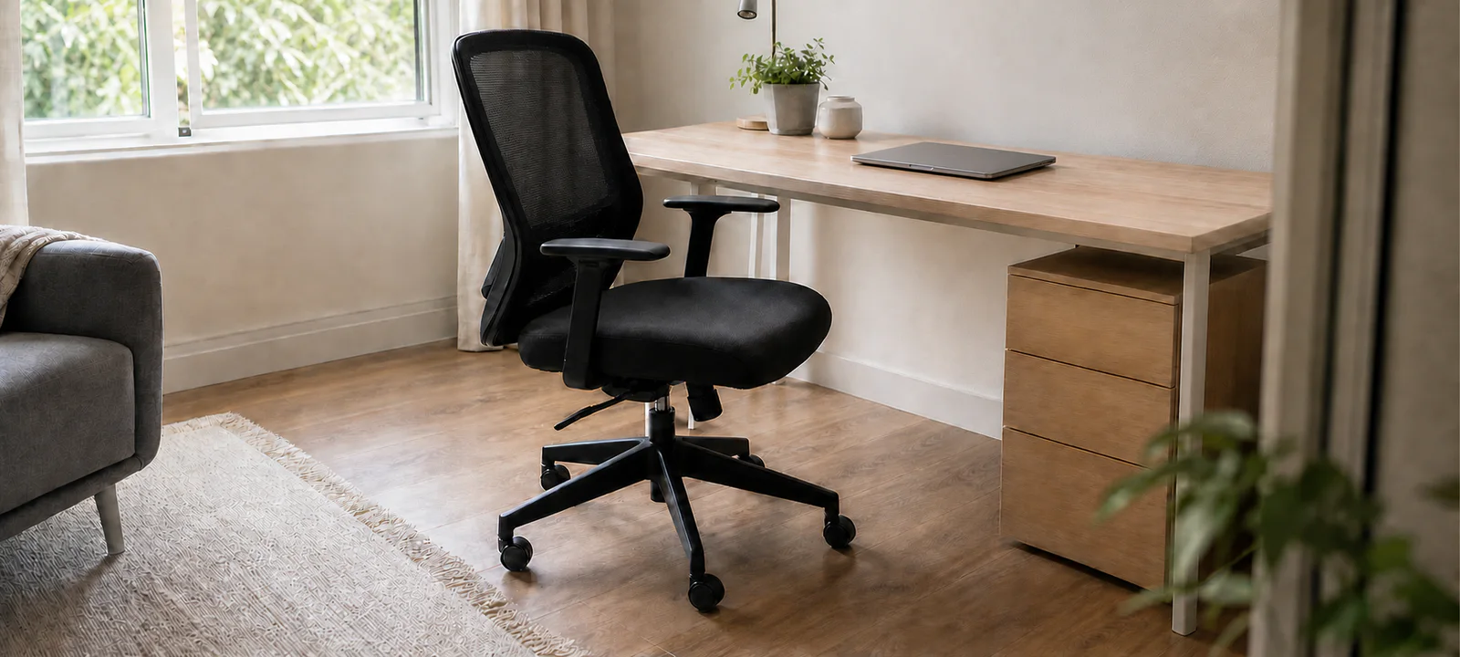 An adjustable mesh office chair with clear pull-out space at a light timber desk in a shared room