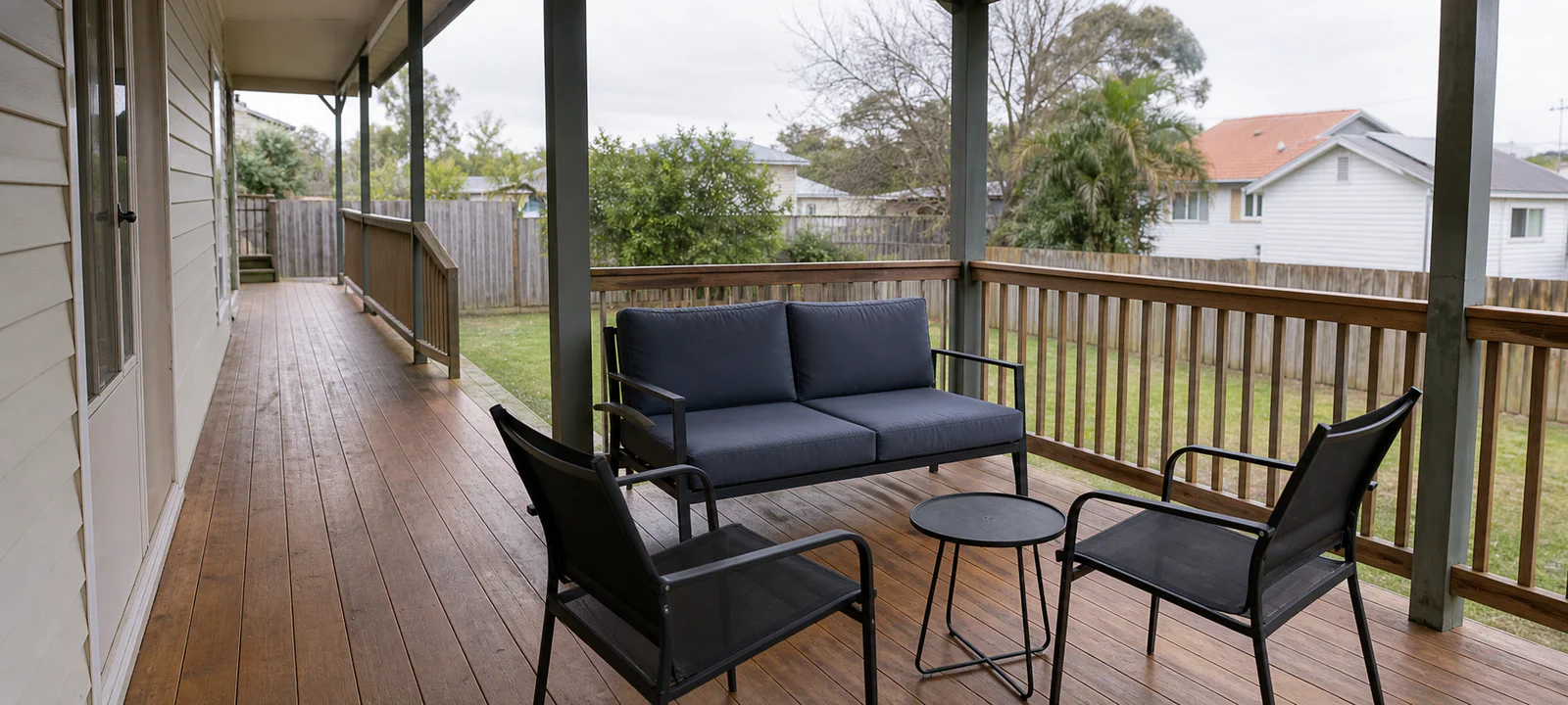 A compact outdoor sofa and two mesh chairs arranged on a covered deck beside a clear walkway